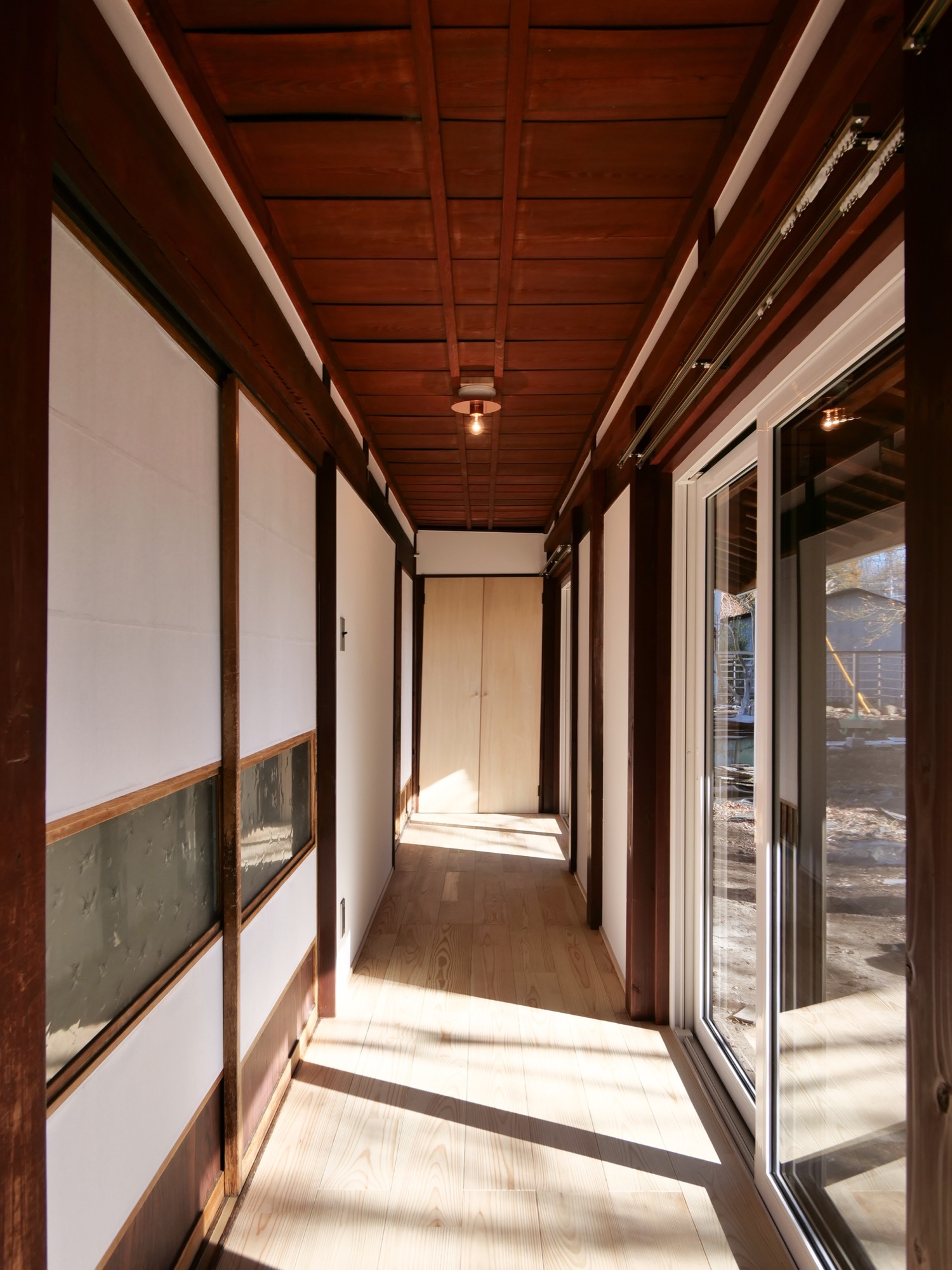 伝統的な和風建築をリノベーションした、自然光が差し込む木造の廊下。障子とフローリング、天井の木組みが調和したモダンな和の空間。